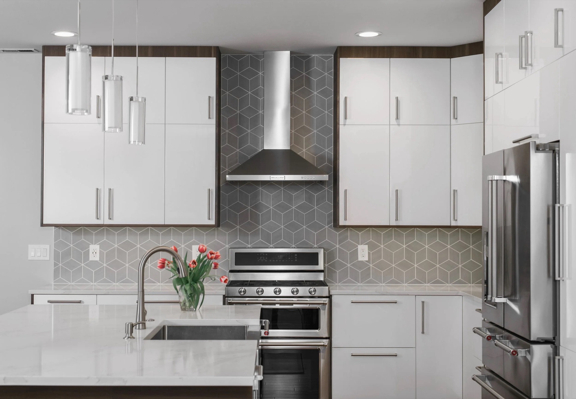Kitchen remodeled by NW Build with white flat-panel cabinetry, a quartz island, tile backsplash and stainless appliances.