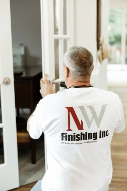 An NW Finishing carpenter in a branded shirt fitting a pair of interior French doors.