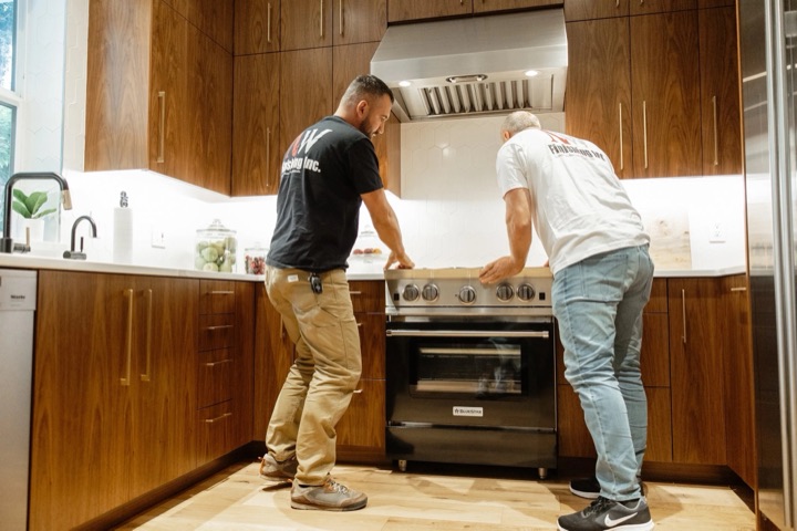 Two NW Finishing carpenters setting a professional range into a walnut kitchen during installation.
