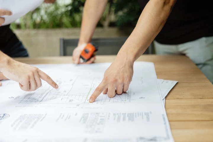 Two people reviewing construction blueprints on a table with a tape measure alongside.