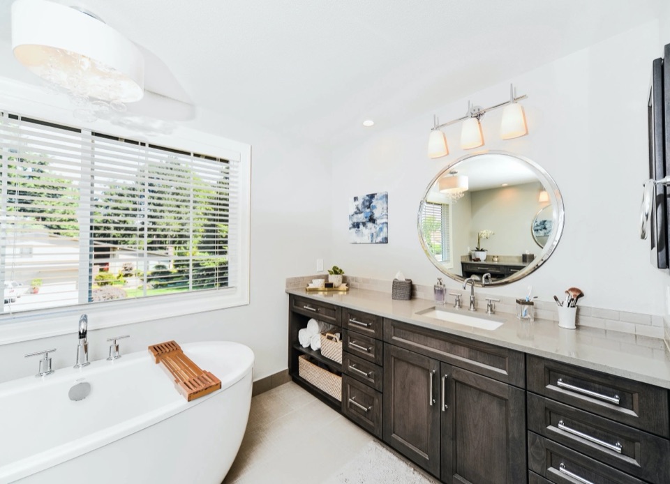Eclectic Traditional in Bellevue: a renovated bathroom with a freestanding tub, dark wood vanity and a round mirror.