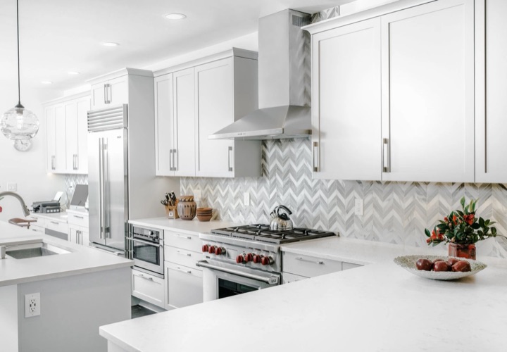 White kitchen with a chevron tile backsplash, professional range and stainless hood.